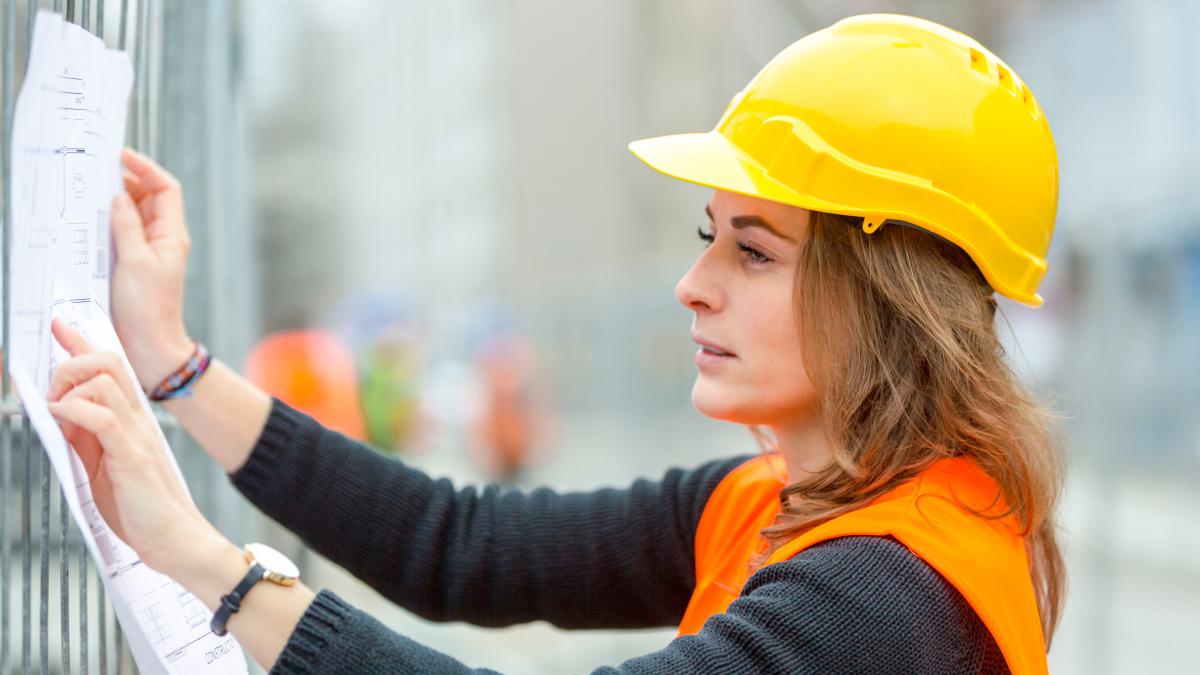 Frau mit Helm und Warnweste schaut sich einen Bauplan an
